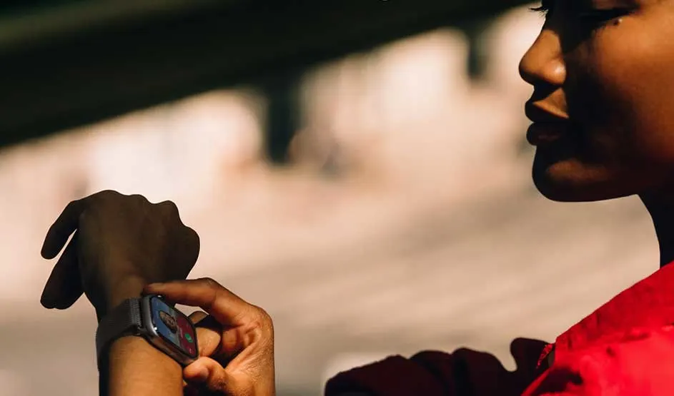 Person in red shirt checking time on smartwatch outdoors in natural sunlight with blurred background.