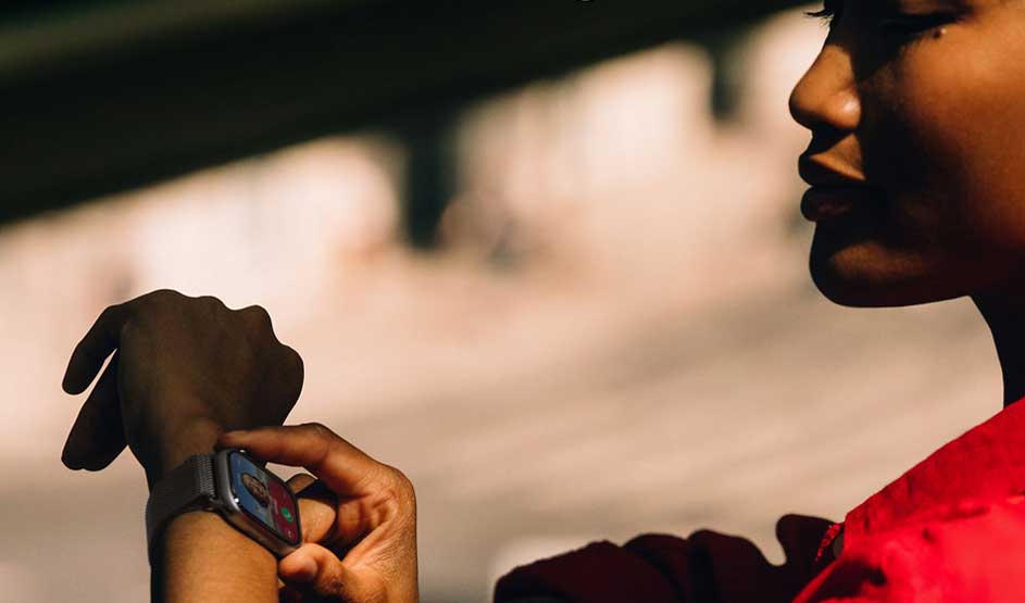 Zijaanzicht van persoon in rood shirt die een smartwatch bedient, met vage achtergrond.