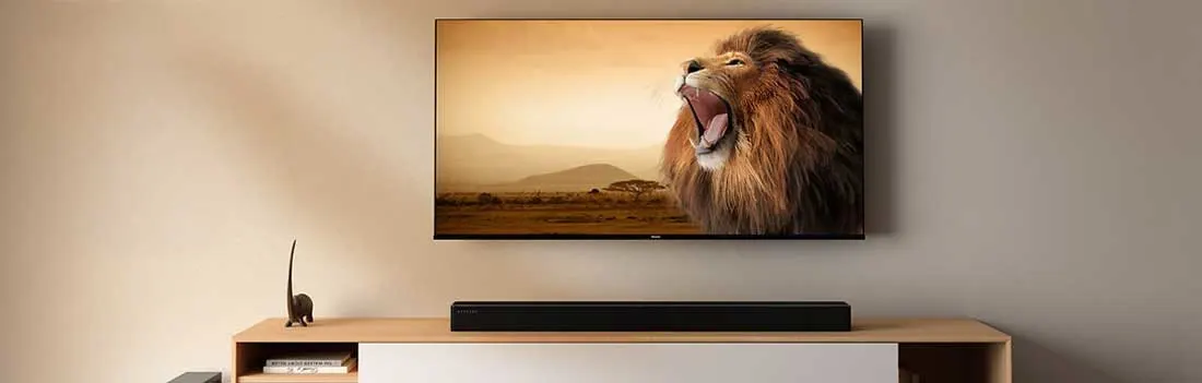 Een grote tv toont een brullende leeuw boven een houten meubel met soundbar; de kamer oogt strak, warm en modern.