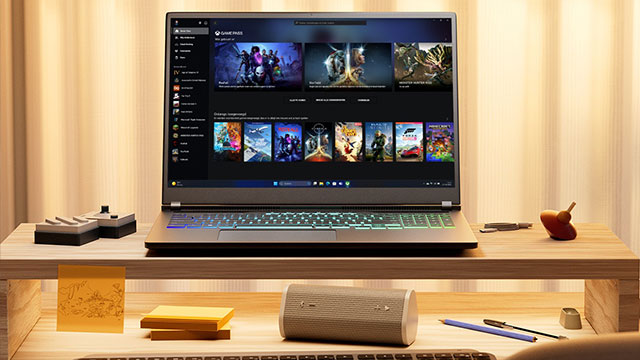 Laptop met games op scherm, naast een controller op een houten bureau met een luidspreker en kantoorbenodigdheden.