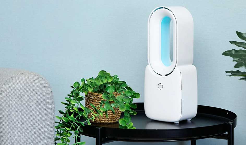 Een Duux ventilator met blauw licht staat op een zwarte tafel naast een plant en een grijze bank in een moderne kamer.