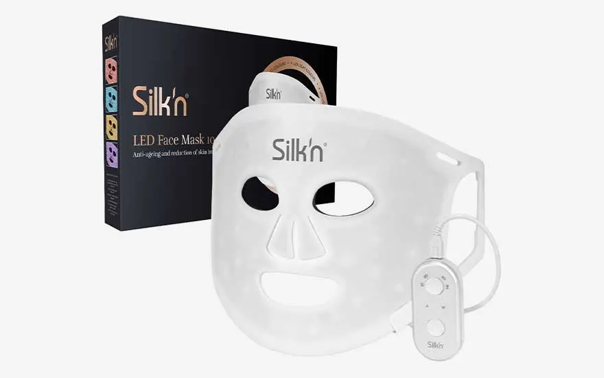 Een witte LED-gezichtsmasker met bedieningskastje staat voor de verpakking op een strakke witte achtergrond.