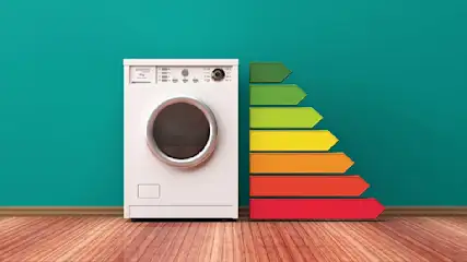 Een wasmachine staat naast een energie-efficiëntielabel met pijlen in groen, geel en rood tegen een blauwe achtergrond op een houten vloer.