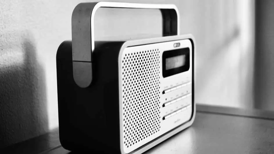 Een zwart-witte foto toont een radio met een handvat en een digitaal display op een tafel.