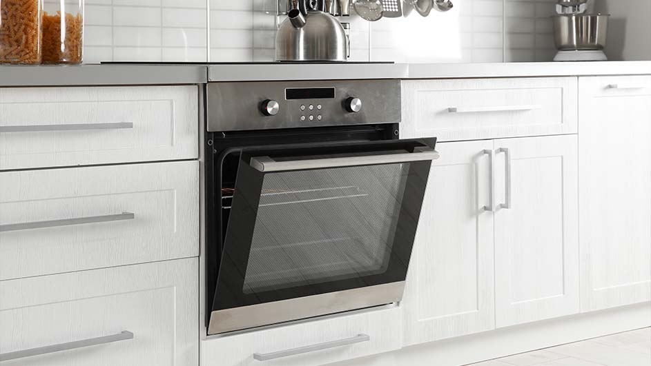 A kitchen features white cabinets, a stainless steel oven with its door ajar, and assorted utensils hanging above.