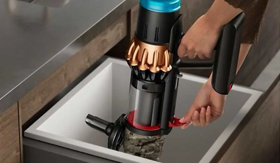 Een persoon leegt de transparante stofcontainer van een Dyson steelstofzuiger boven een prullenbak met één simpele rode hendel.