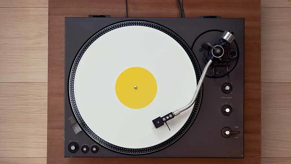 Platenspeler op een houten ondergrond met een witte plaat en een geel label in het midden.