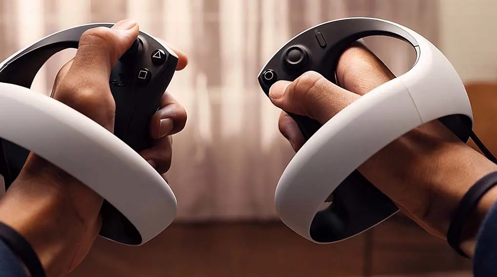 Two hands hold black and white VR controllers. The left controller has buttons, and the right one has a joystick.