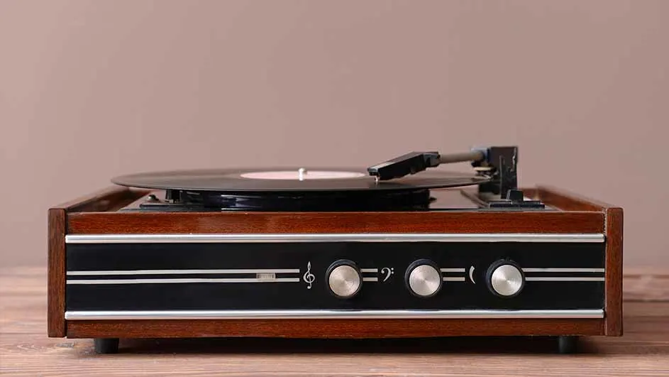 Houten platenspeler met zwarte plaat, toonarm en zilverkleurige bedieningsknoppen op een houten ondergrond.