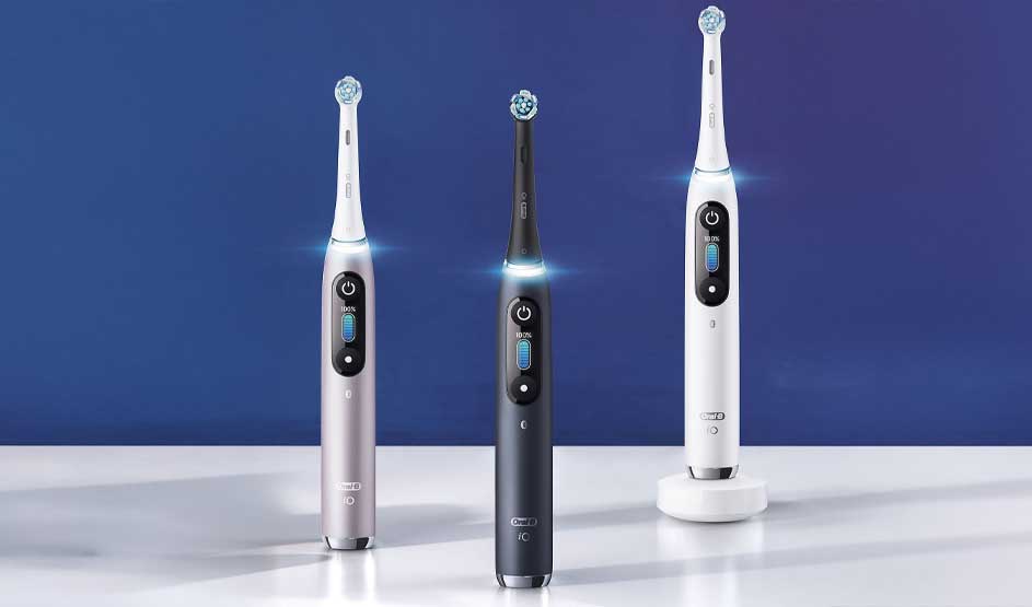 Three sleek Oral-B electric toothbrushes stand on a glossy white surface, softly illuminated before a smooth blue background.