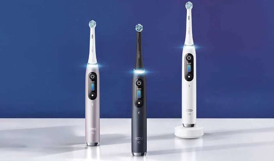 Drie moderne elektrische Oral-B tandenborstels staan rechtop op een glanzend wit oppervlak, verlicht tegen een strakke blauwe achtergrond.