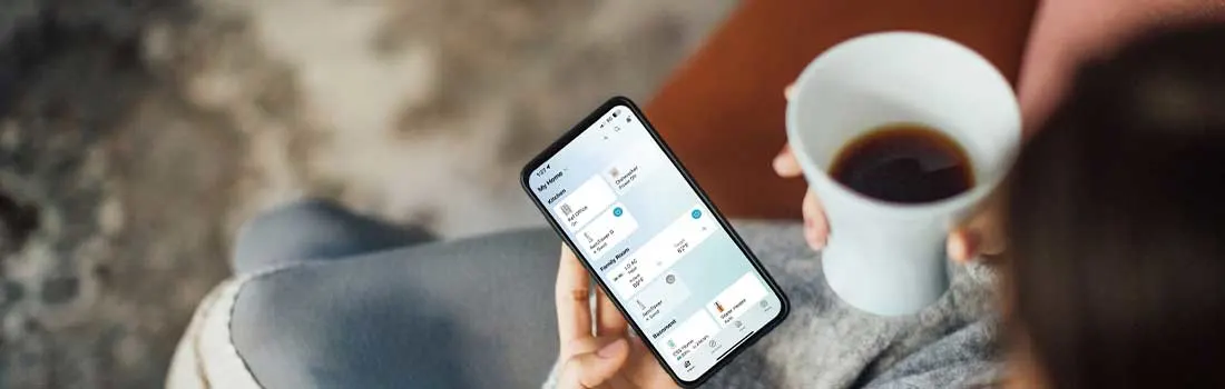 Persoon ontspant met koffie en bekijkt de LG ThinQ-app op een smartphone voor verbonden apparaten thuis.