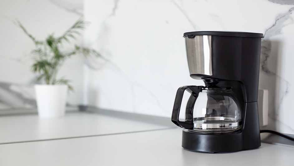 Filter coffee machine on a light kitchen counter with a plant in the background.