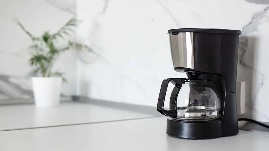 Filter coffee machine on a light kitchen counter with a plant in the background.