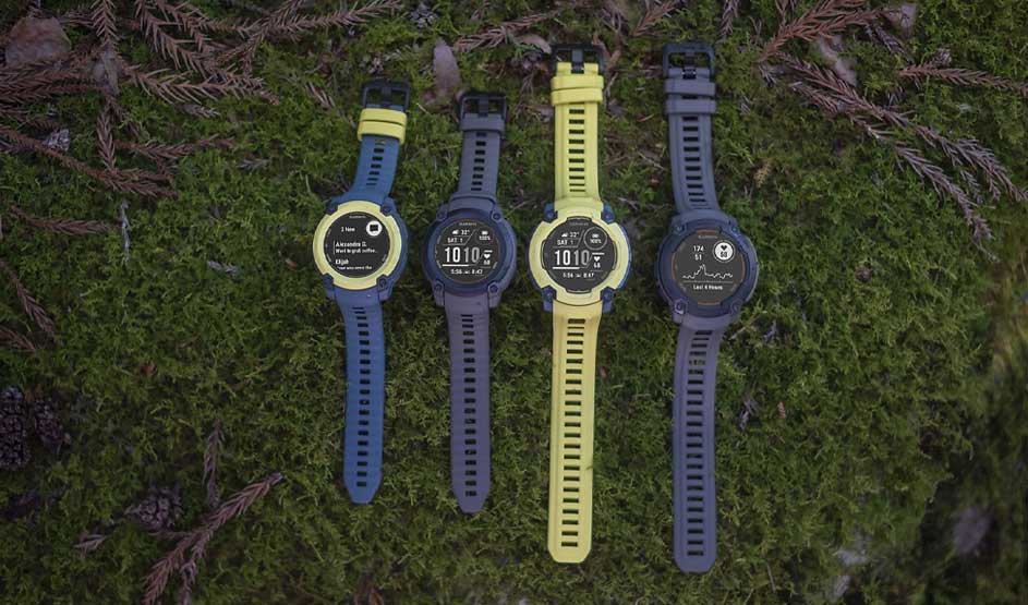 Four sports watches with yellow and blue straps displayed on moss, showing different digital watch faces and data screens.