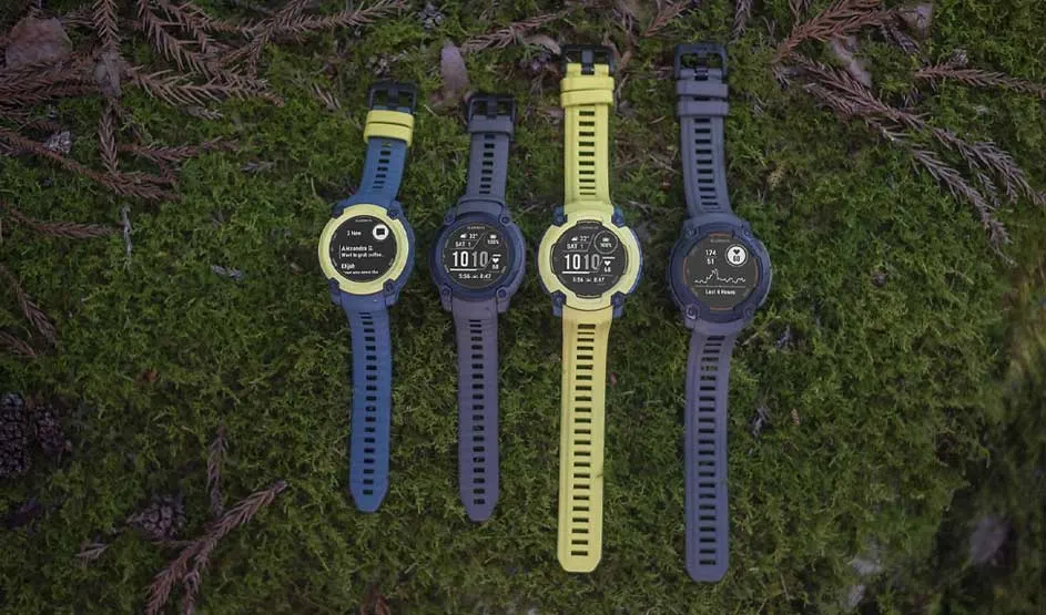 Four sports watches with yellow and blue straps displayed on moss, showing different digital watch faces and data screens.