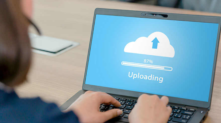 Een persoon typt op een laptop met een blauw scherm waarop een witte cloud met een pijl en "Uploading 87%" staat.