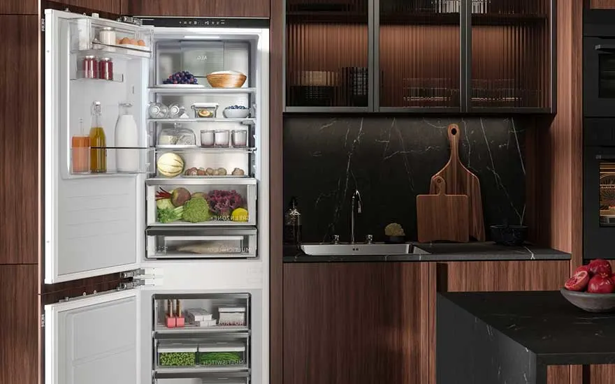 An AEG fridge, filled with fruit, vegetables, juice, and dairy, stands open in a luxury kitchen with dark wood and black marble surfaces.