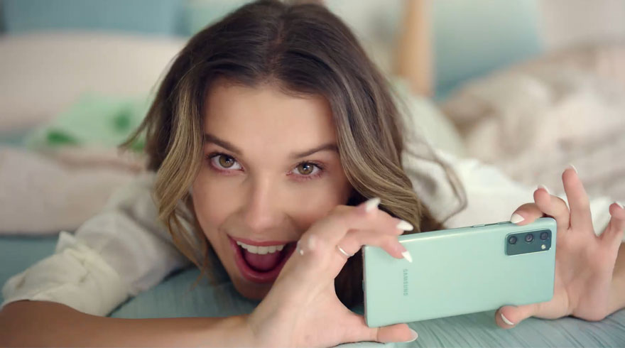 Vrouw ligt op een bed met een mintgroene telefoon in haar handen en een lachende gezichtsuitdrukking.