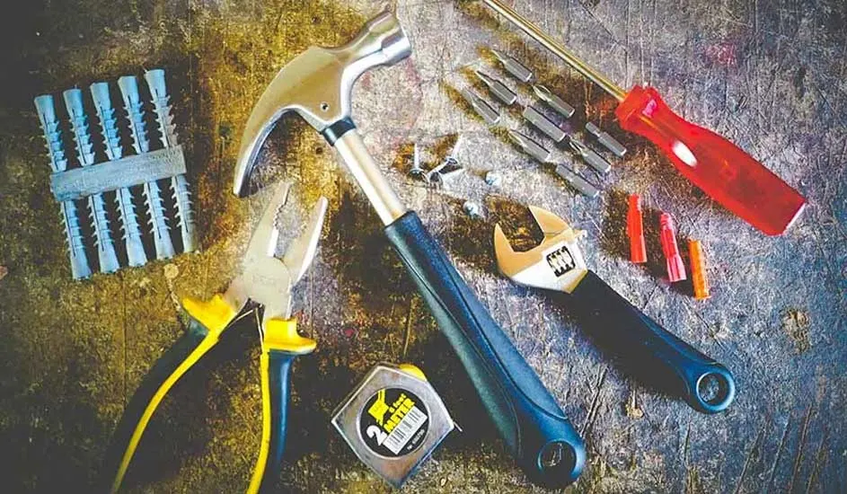 Tools including a hammer, pliers, screwdriver, wrench, tape measure, anchors and screws on a textured surface.