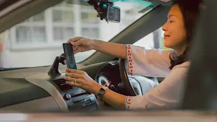 Een vrouw plaatst een zwarte smartphone in een autohouder op het dashboard van een auto.