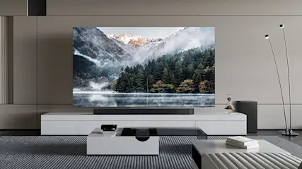 Een woonkamer met een grote tv met een berglandschap, witte kasten en tafels op een gestreepte vloerkleed.
