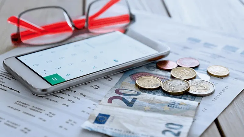 Bril, telefoon met rekenmachine, muntgeld en een biljet van 20 euro op een document.