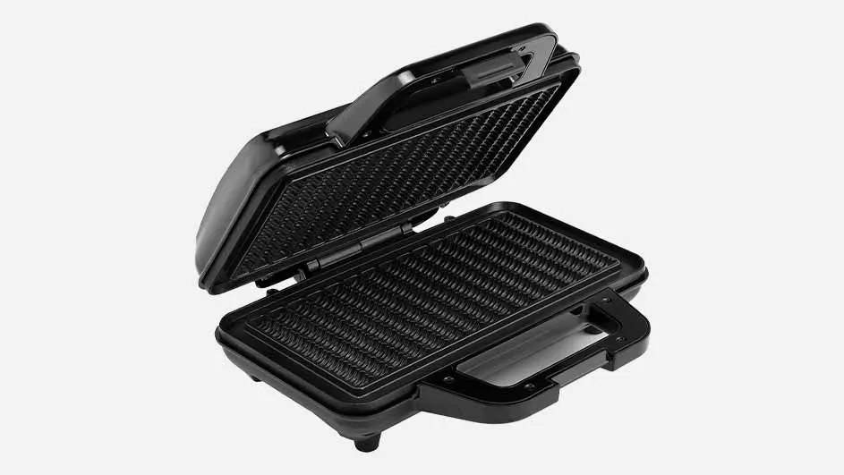 Een zwarte, opengeklapte panini-grill met ribbels staat op een witte achtergrond.
