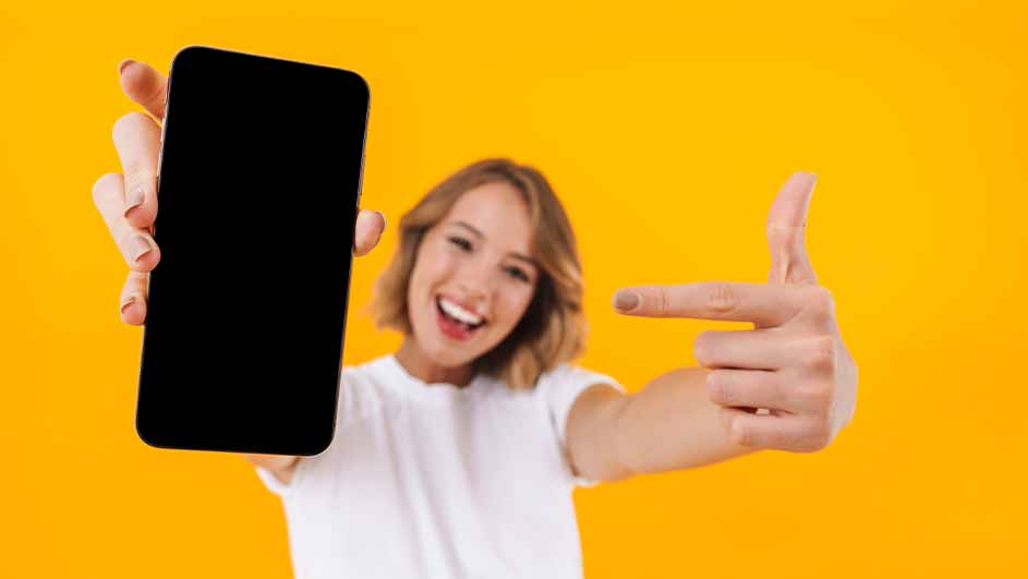 Vrouw in wit shirt wijst naar een zwarte smartphone tegen een gele achtergrond.