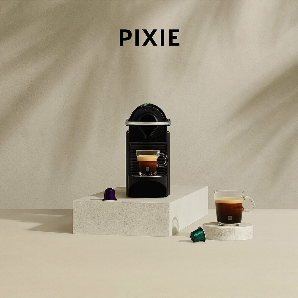 Een zwarte Nespresso Pixie machine met koffie in een kopje, capsules en de tekst "PIXIE" op een beige achtergrond.