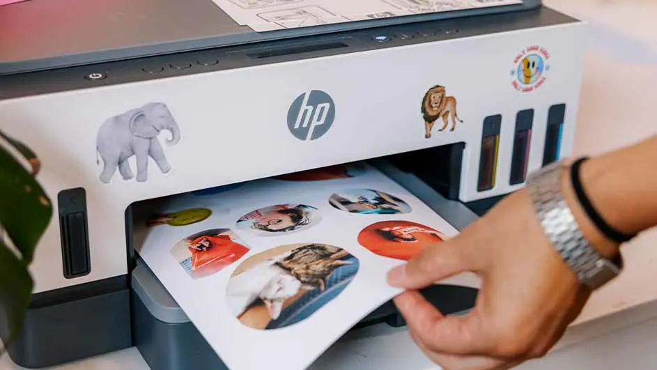 Een printer met stickers van een olifant en een leeuw. Een hand trekt een blad met ronde afbeeldingen uit de printer.