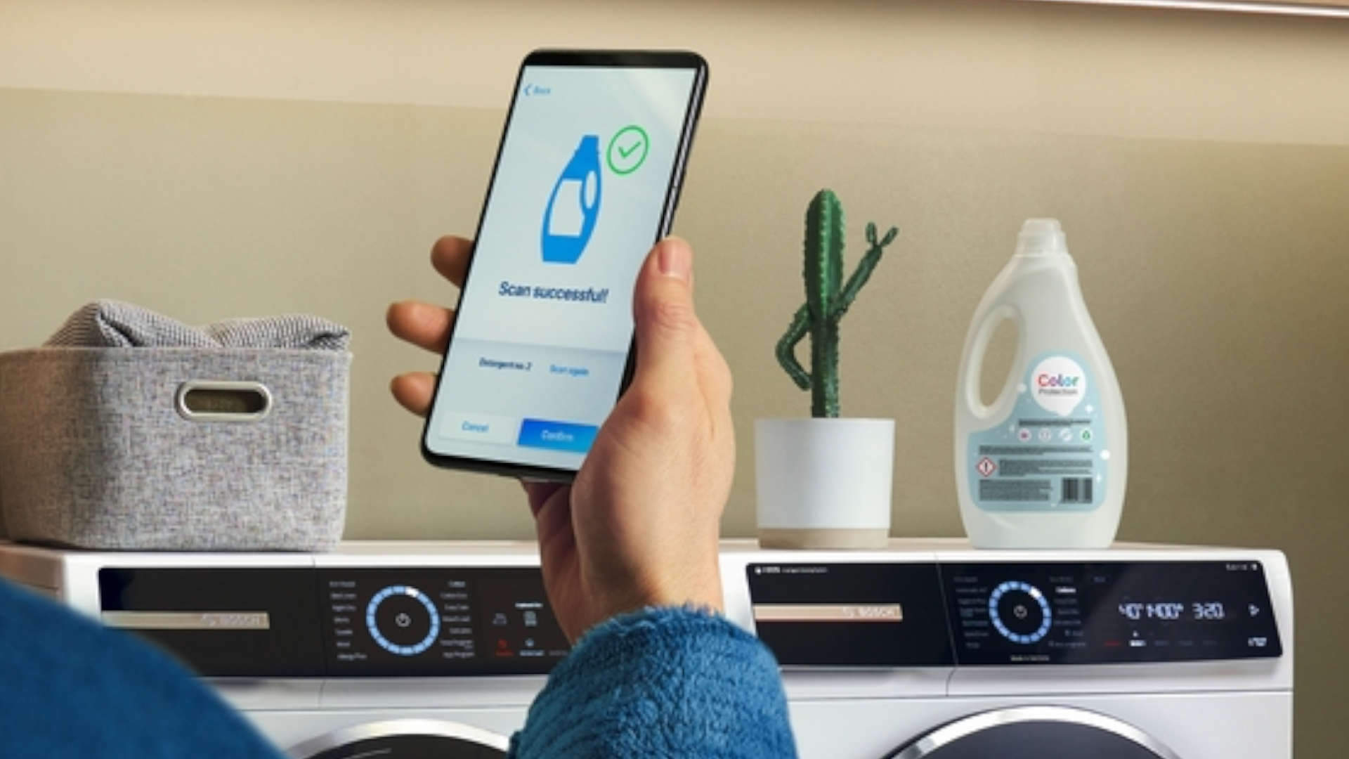 Wasmachine met smartphone die een scan-succesbericht toont, naast een wasmiddelcontainer en een cactus in een witte pot.