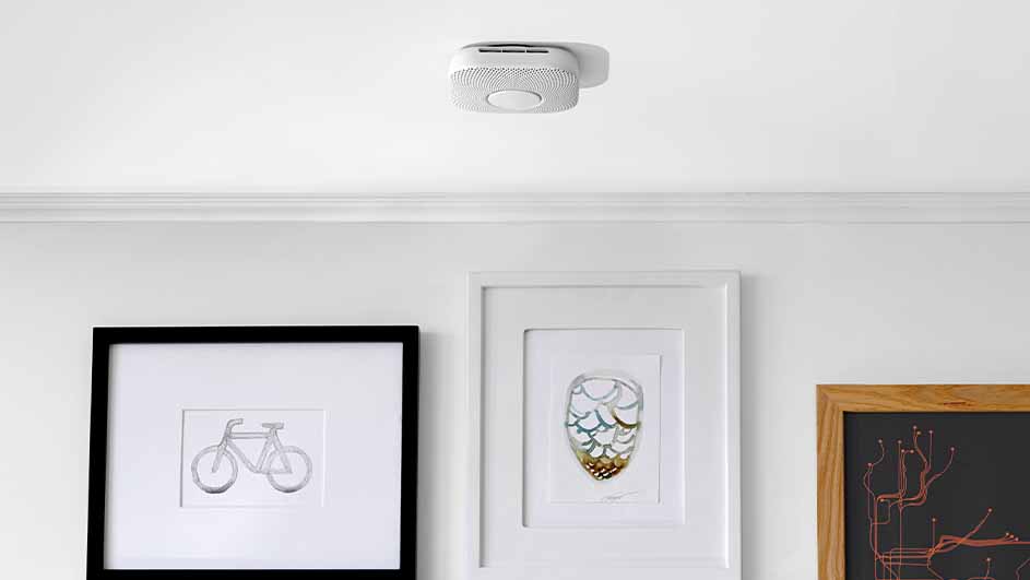 A white ceiling features a round smoke detector. Below, three framed artworks hang on a white wall.