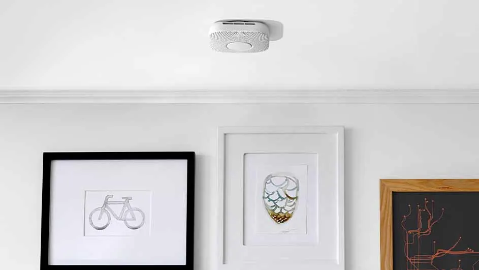 A white ceiling features a round smoke detector. Below, three framed artworks hang on a white wall.