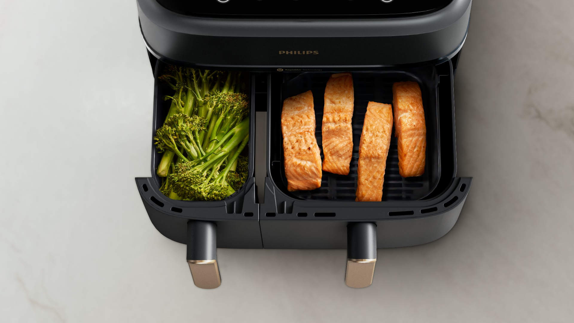Een zwarte Philips Airfryer met broccoli en zalm in de compartimenten, klaar om te koken.