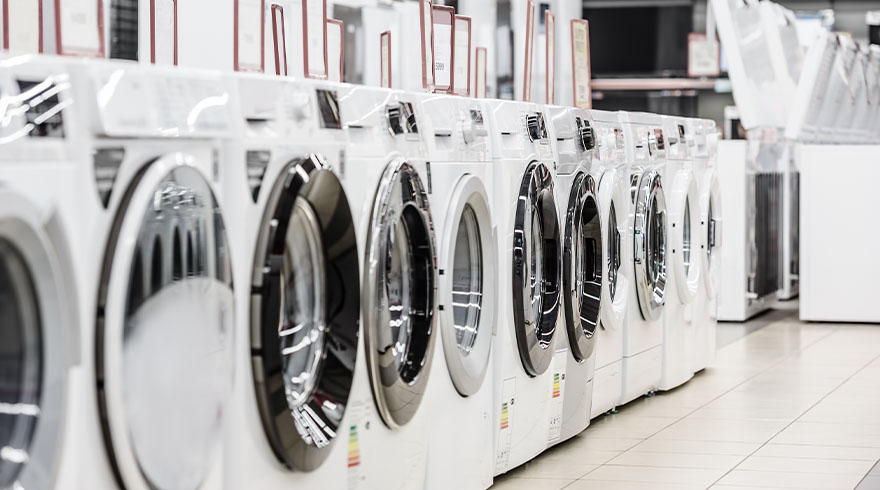 Rij witte wasmachines met ronde deuren staan op een rij in een winkel, klaar voor verkoop.