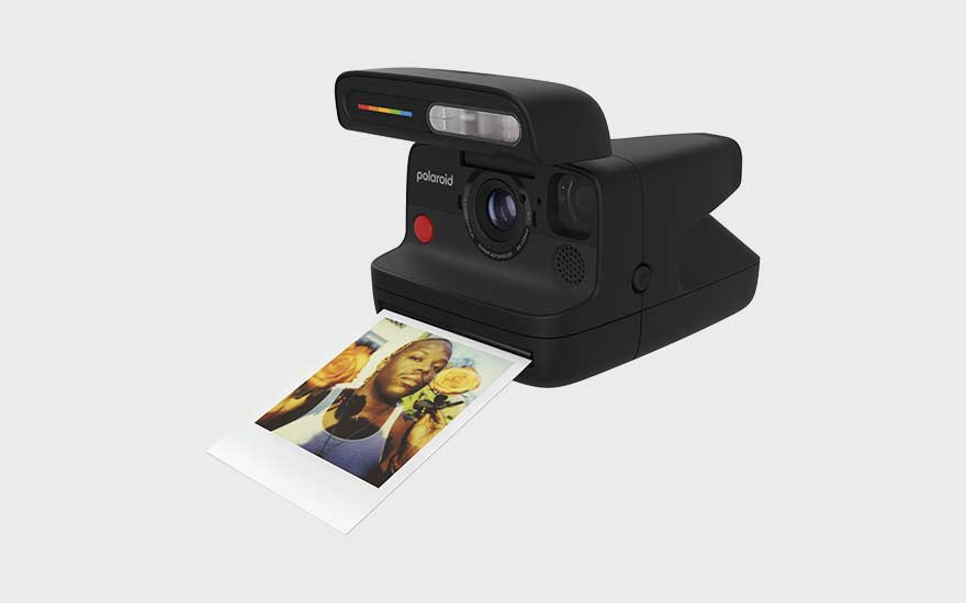 Een zwarte Polaroid-camera print een foto meteen uit. De camera staat schuin op een lichte ondergrond met een kleurrijke foto.