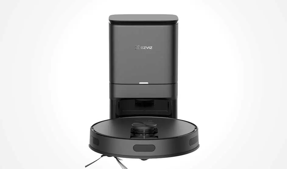 Een zwarte robotstofzuiger staat voor een hoog, rechthoekig basisstation; studio-opname op wit met gladde afwerking en sensor bovenop.