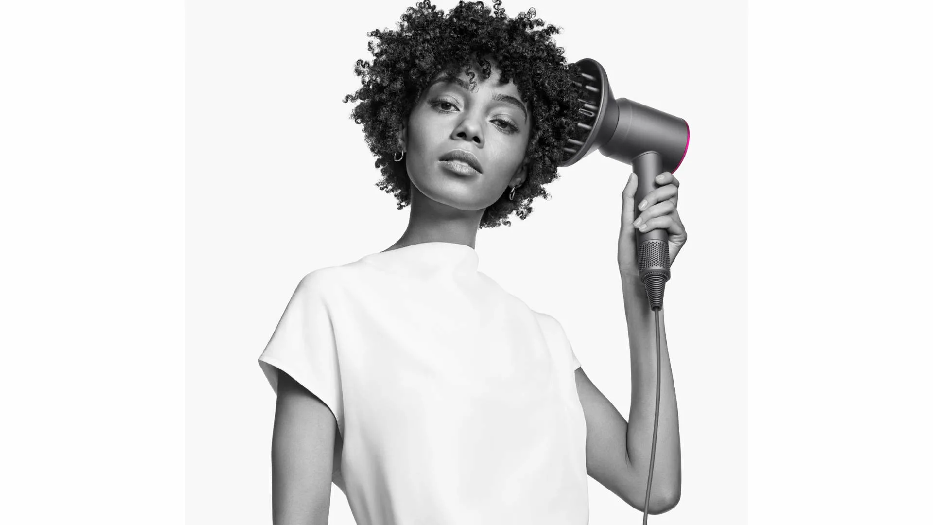 Een vrouw houdt een grijze föhn met een roze accent vast tegen een witte achtergrond.