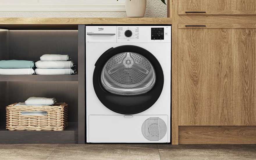 Een moderne beko wasdroger ingebouwd in een houten kast, met opgevouwen handdoeken en een mand ernaast in een stijlvolle wasruimte