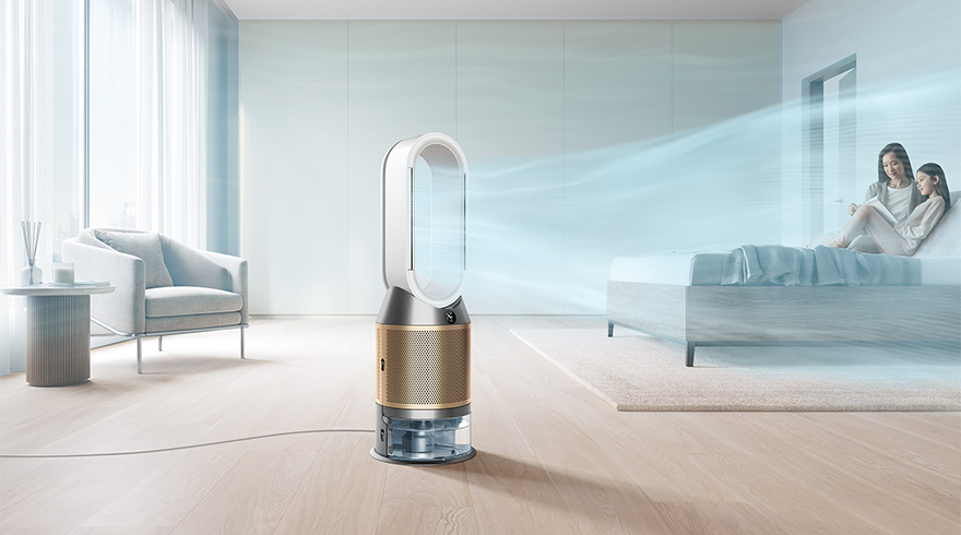 Een kamer met een witte stoel en een tafel bij een raam, een ventilator en twee vrouwen op een bed.