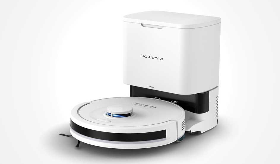 Een witte robotstofzuiger met ronde sensor staat voor een hoog dockingstation met opvangbak; alles is strak gefotografeerd op wit.