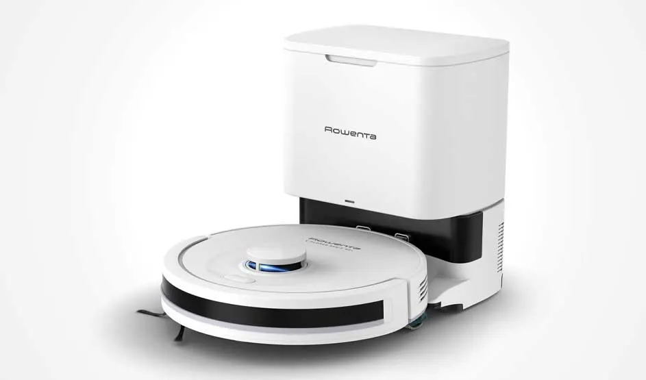 Een witte robotstofzuiger met ronde sensor staat voor een hoog dockingstation met opvangbak; alles is strak gefotografeerd op wit.