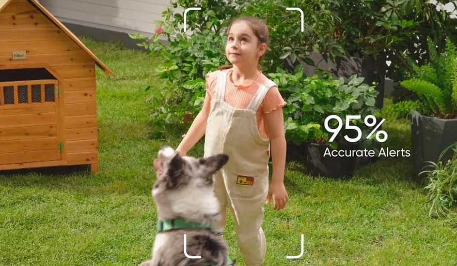 Een kind in lichte tuinbroek staat in de tuin naast een houten hondenhok en speelt met een hond. Rechts staat "95% Accurate Alerts" in beeld.