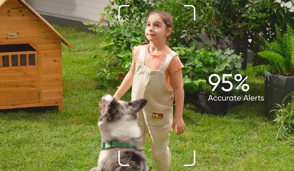 Een kind in lichte tuinbroek staat in de tuin naast een houten hondenhok en speelt met een hond. Rechts staat "95% Accurate Alerts" in beeld.