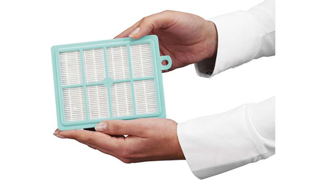 Een persoon in een wit overhemd houdt een rechthoekig, turquoise filter met witte plooien vast.