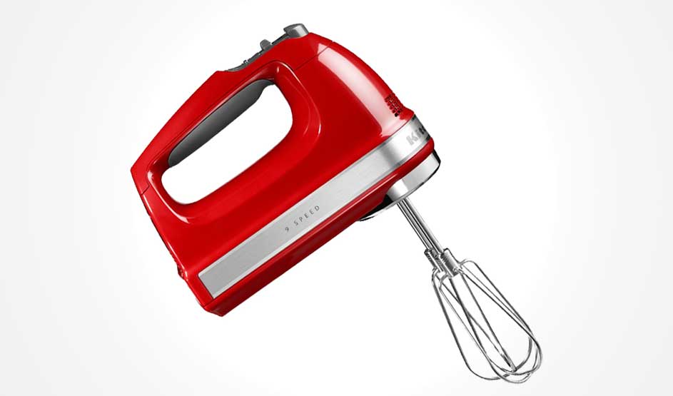 Een rode handmixer met metalen garde staat schuin tegen een witte achtergrond; je ziet de handgreep, snelheidsknop en glanzende afwerking.