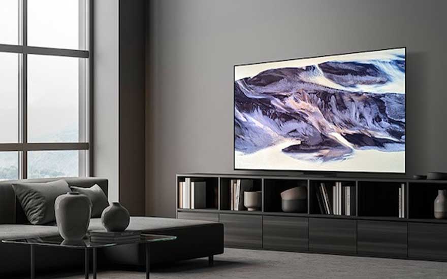 Een moderne, minimalistische woonkamer met grijze tinten, een grote tv aan de muur toont abstracte kunst, veel natuurlijk licht.