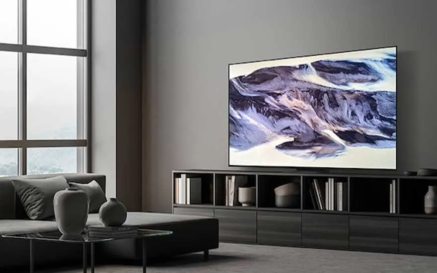 Een moderne, minimalistische woonkamer met grijze tinten, een grote tv aan de muur toont abstracte kunst, veel natuurlijk licht.