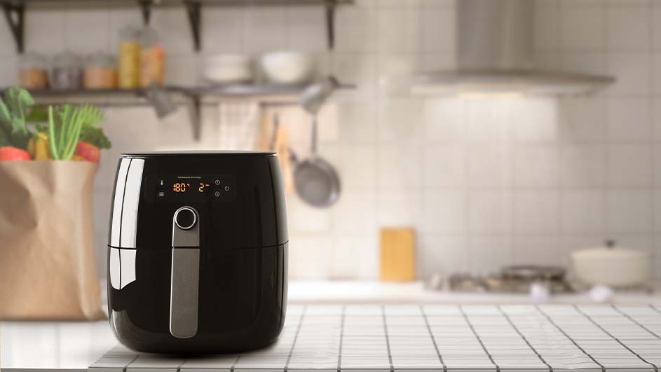 Black air fryer on a tiled kitchen counter, set to 180 degrees, with cooking utensils and vegetables in the background.